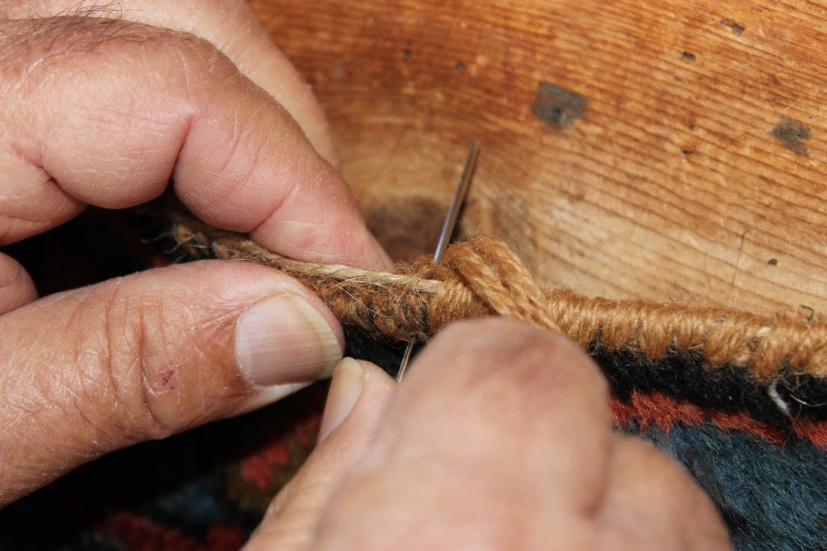 Hand repairing a traditional rug with needle and thread at Zeytounian Rugs San Diego, CA.