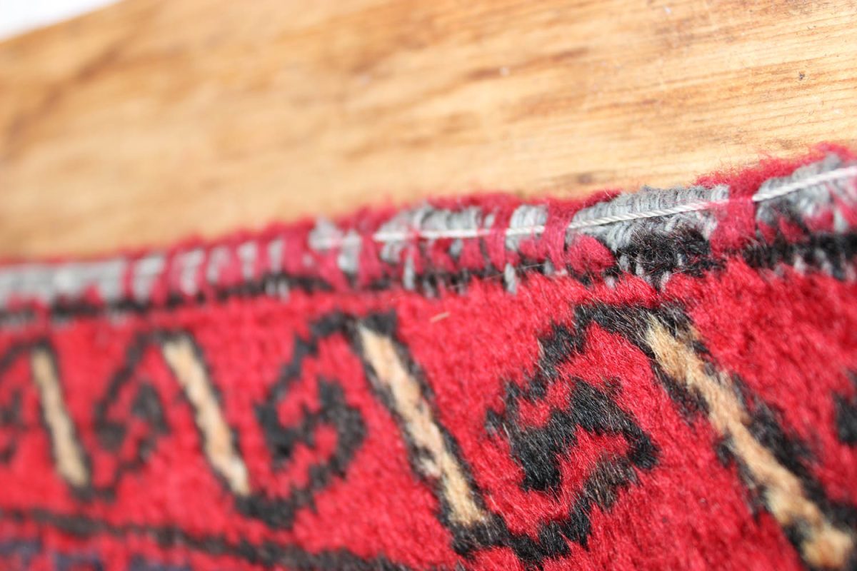 Worn overcast binding on the edge of a red patterned rug