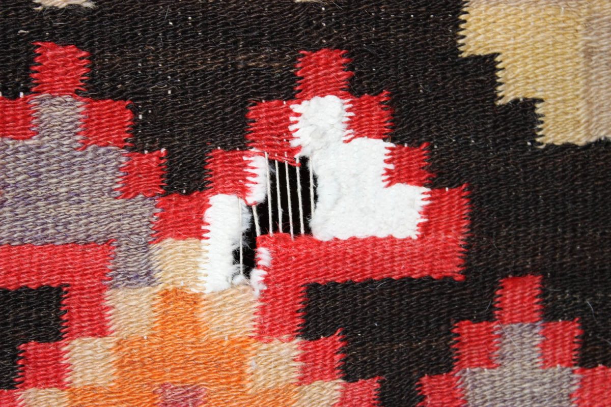 Vintage Persian rug with visible damage and repair stitches.