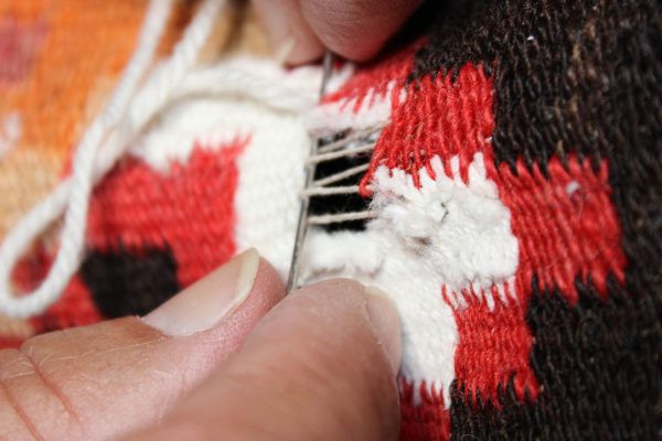 Hand repairing a colorful woven rug with a needle and thread.