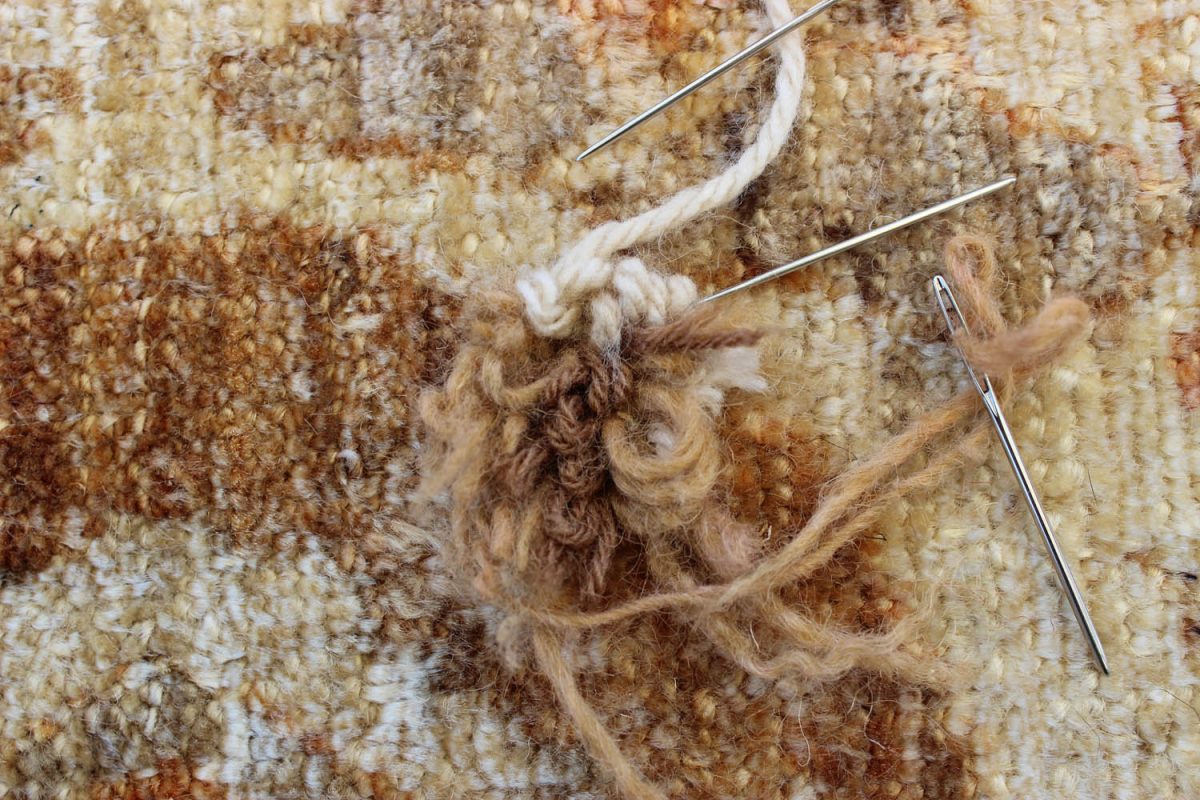 Wool rug repair with sewing needles and yarn on textured carpet.