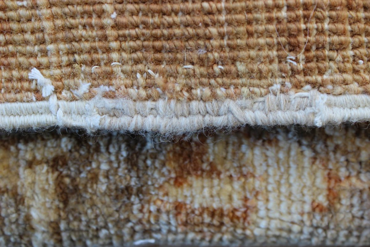 Close-up of a worn and stained rug showing frayed edges and damaged fibers.