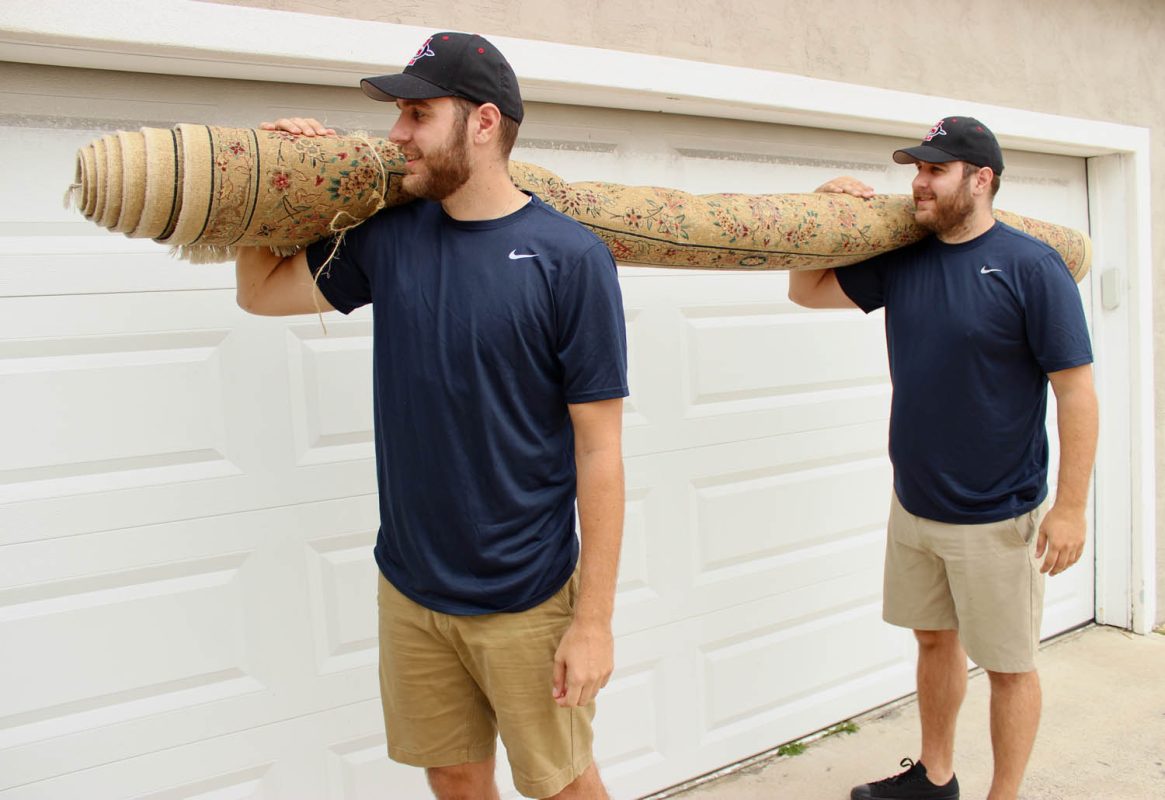 Man carrying a large decorative rug on his shoulder.