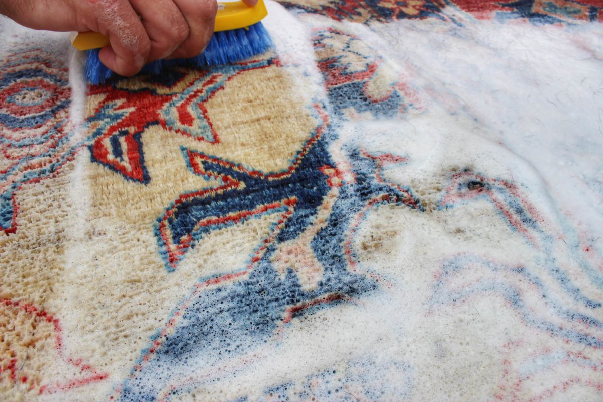 Antique Persian rug being cleaned with a brush and foam for deep dirt removal.