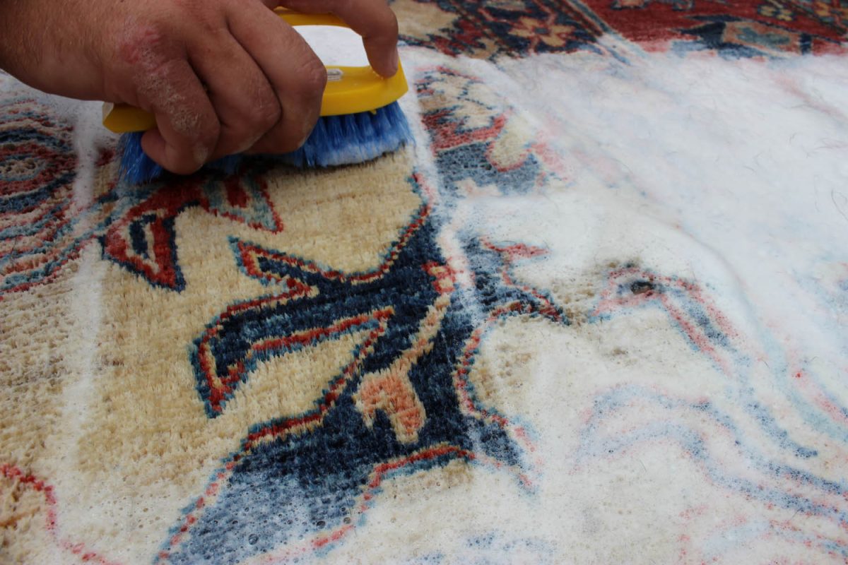 Hand cleaning a traditional Persian rug with a brush in a professional rug cleaning process.
