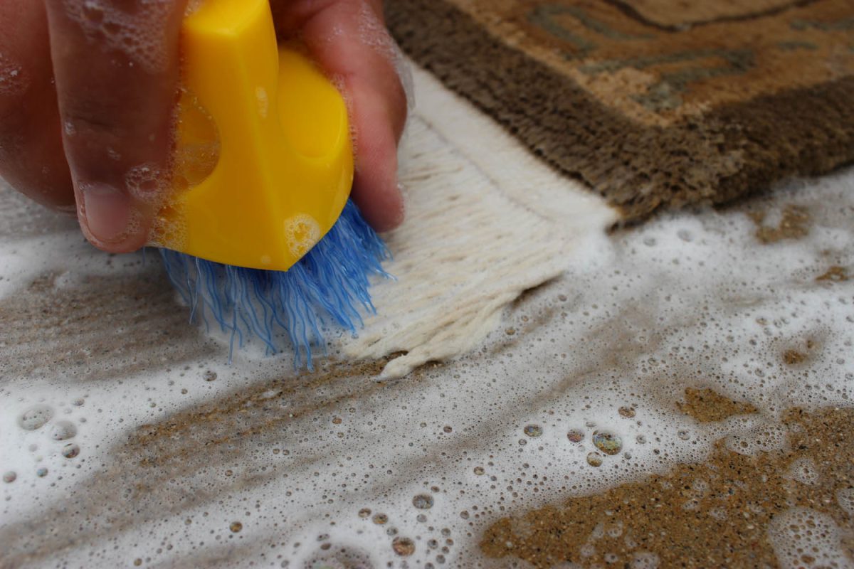 Scrub brush cleaning the white fringe of a wool rug over soiled washing foam
