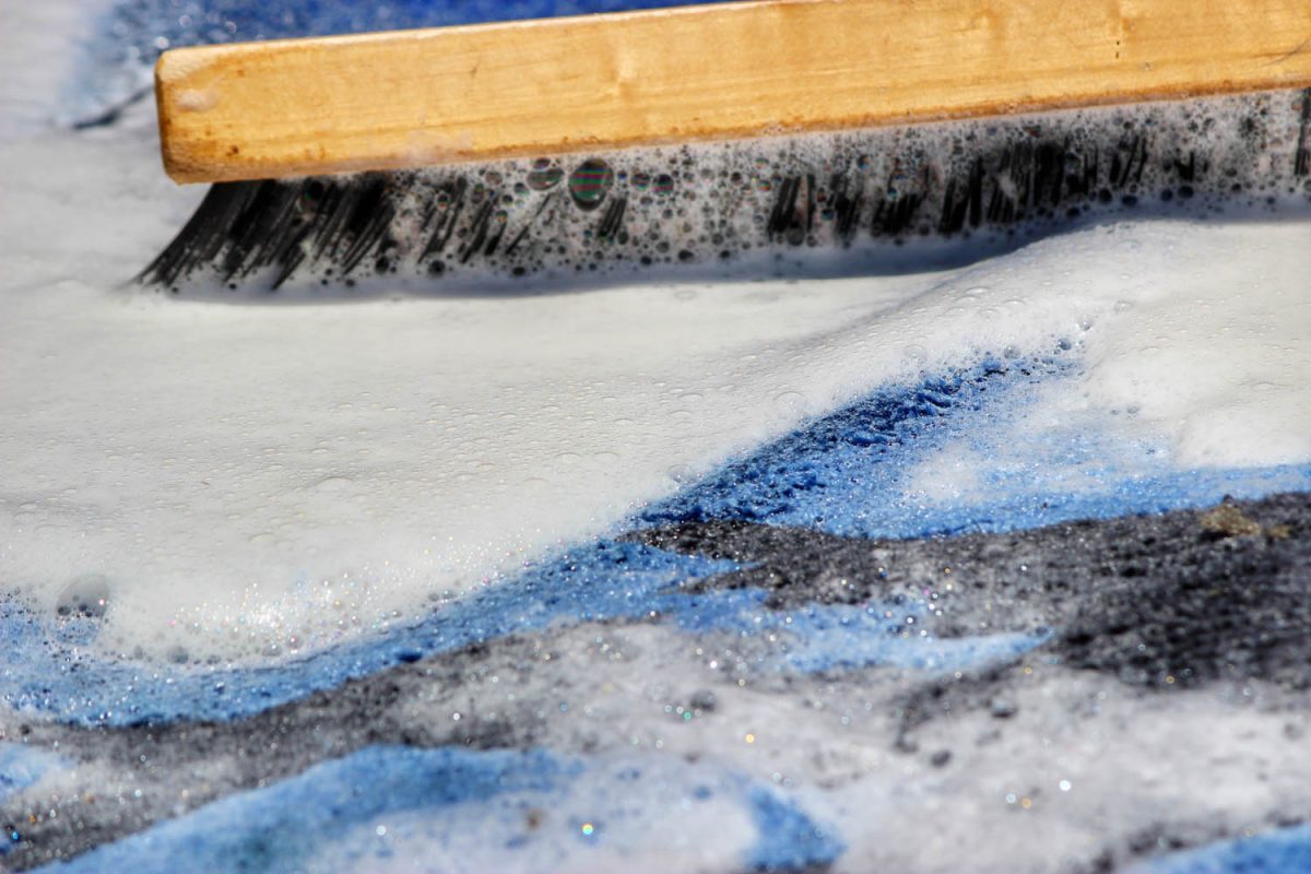 Rug cleaning process with a brush on a soapy rug surface in San Diego.