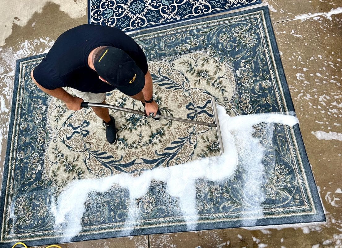 Rug cleaning technician applying foam to a traditional Persian rug for deep cleaning.