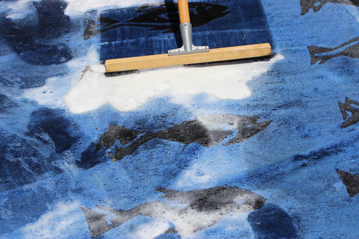 Squeegee pushing foam across a blue rug patterned with fish